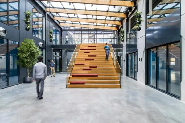 Moderne en lichte kantoorruimte aan de Laarderhoogtweg met een brede houten tribunetrap, glazen dak en meerdere mensen in beweging.