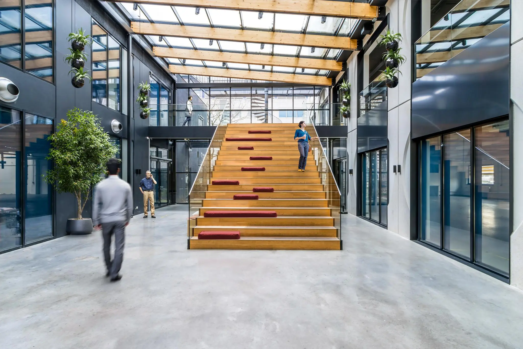 Moderne en lichte kantoorruimte aan de Laarderhoogtweg met een brede houten tribunetrap, glazen dak en meerdere mensen in beweging.