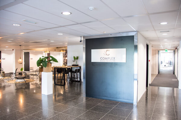 Moderne, lichte kantoorlobby aan de Meidoornkade met zitgedeelte, planten en een bord met het logo "Complex Built to Work".