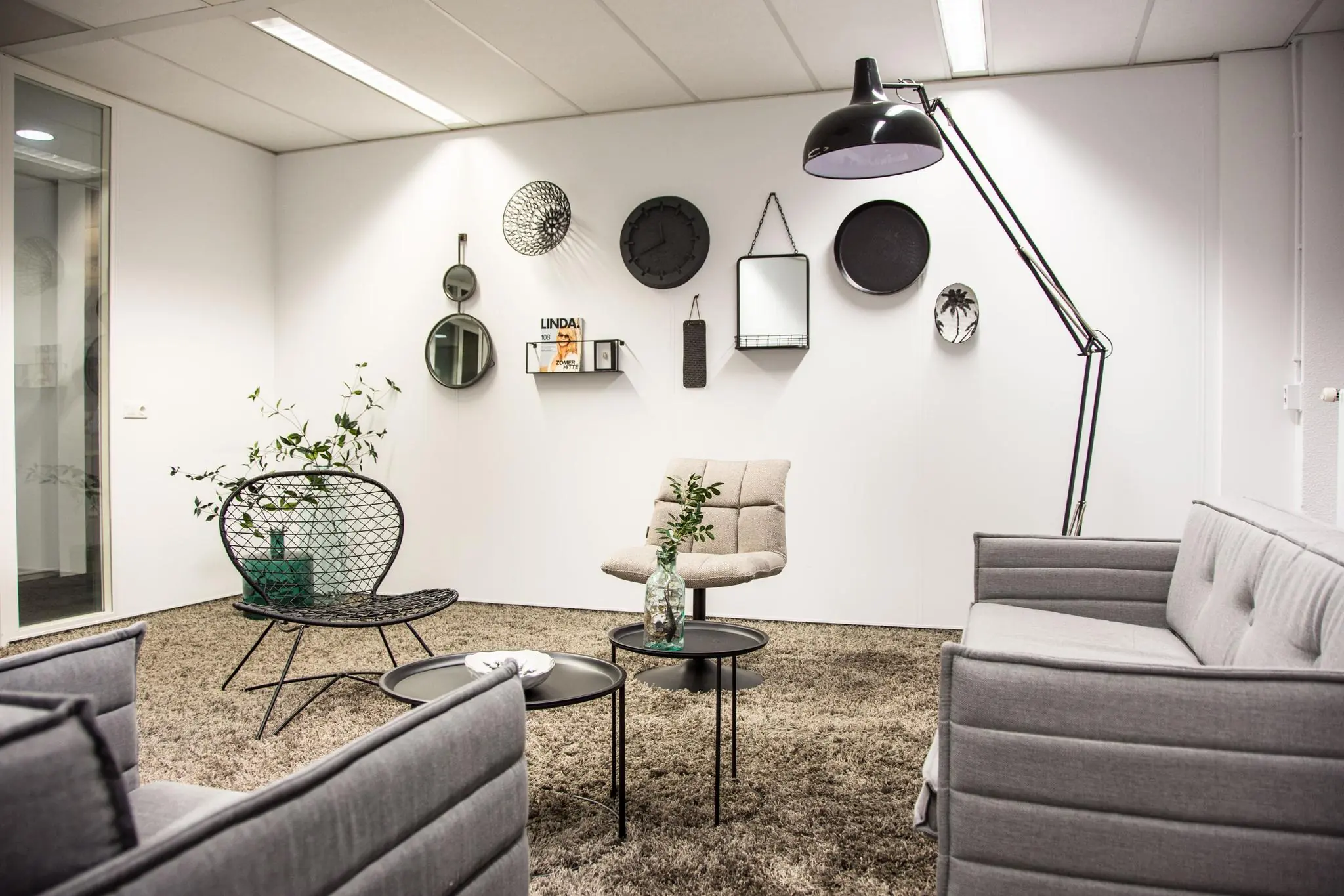 Modern ingerichte wachtruimte aan de Meidoornkade met grijze meubels, wanddecoratie en een grote vloerlamp.