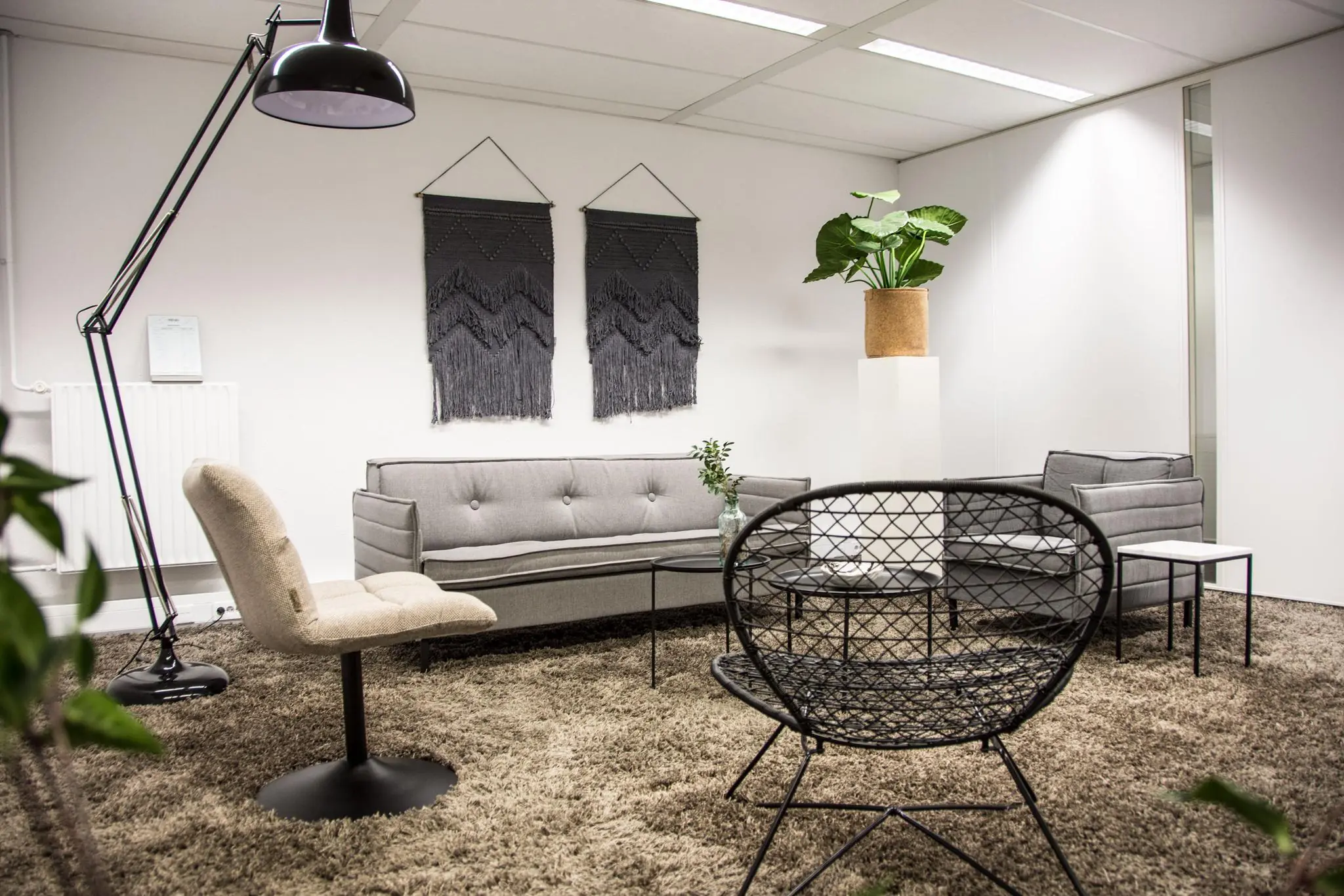 Stijlvolle wachtruimte aan de Meidoornkade met moderne zithoek, vloerkleed, kamerplant en wanddecoratie.
