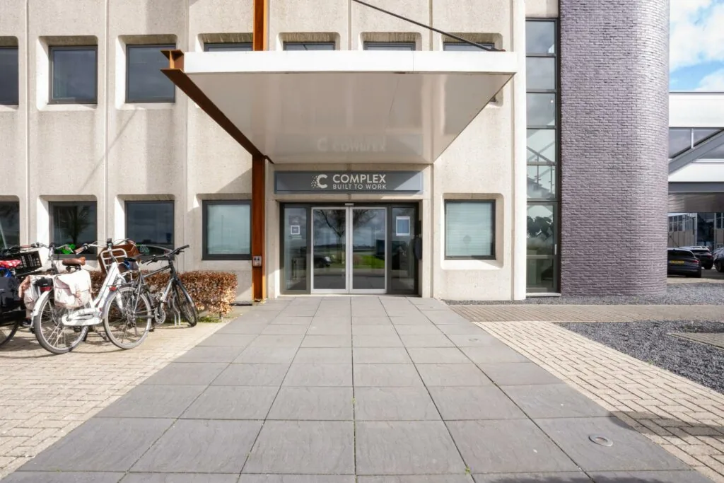Ingang van het kantoorgebouw aan de Meidoornkade met het bord "Complex Built to Work" boven de deur en fietsen geparkeerd links van de entree.