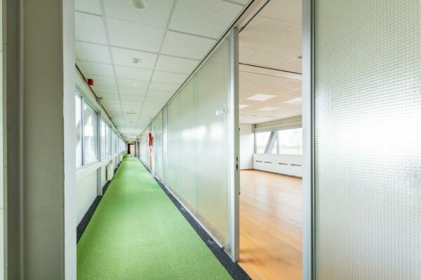 Licht en modern kantoorinterieur aan de Meidoornkade met groene gangvloer en glazen wanden.
