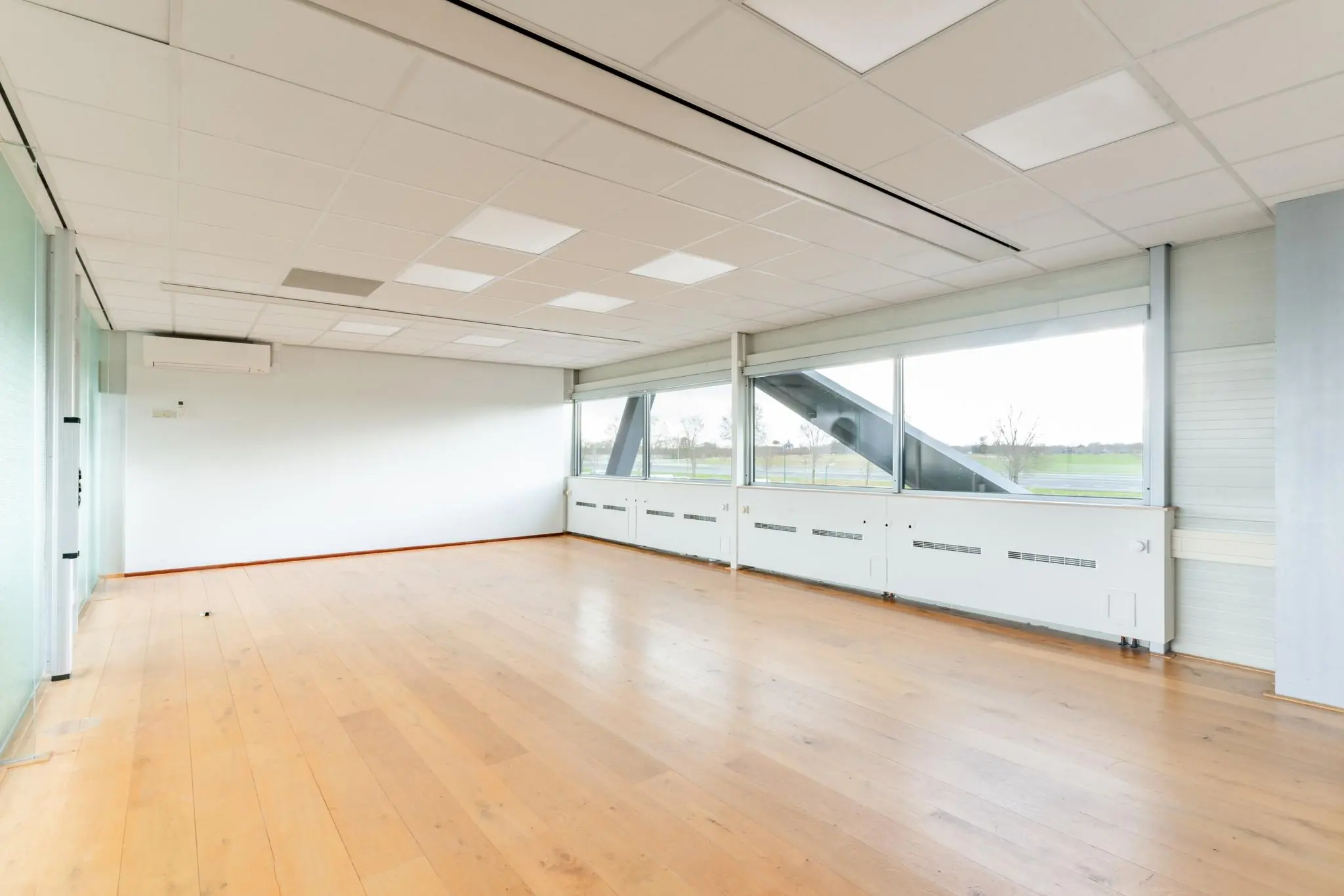 Licht en leeg kantoorruimte aan de Meidoornkade met houten vloer en grote ramen met uitzicht op groen landschap.