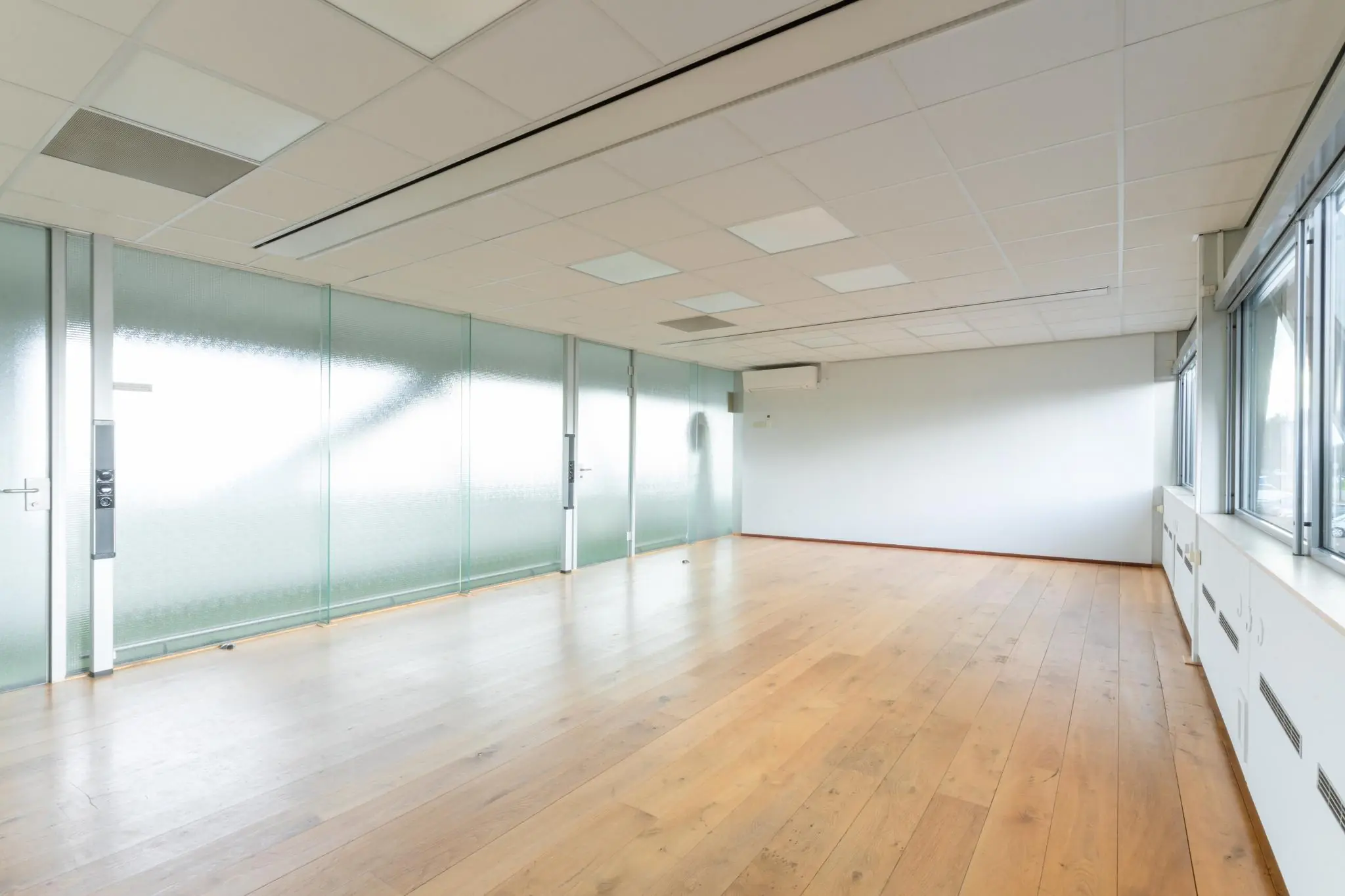 Lichte, lege kantoorruimte aan de Meidoornkade met glazen wand en houten vloer.