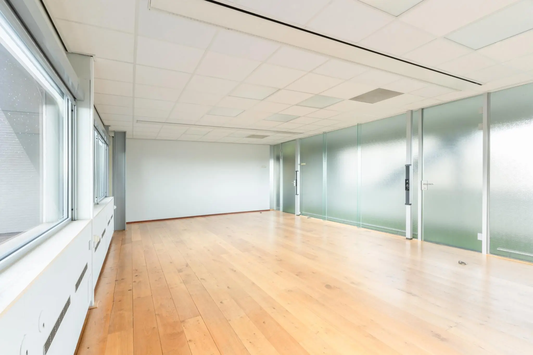 Lichte, lege kantoorruimte aan de Meidoornkade met houten vloer en glazen wanden.