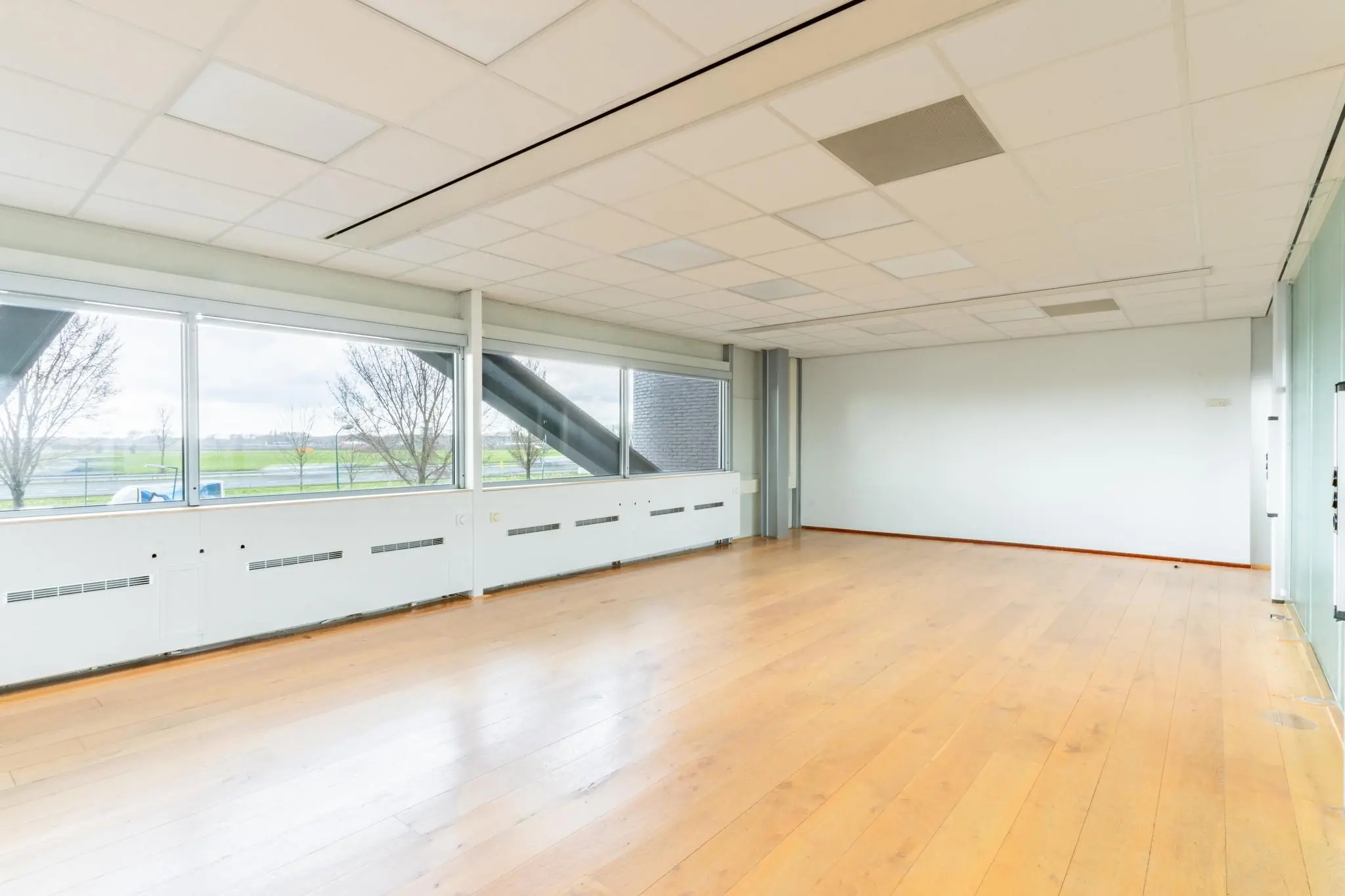Lichte, lege kantoorruimte aan de Meidoornkade met houten vloer en grote ramen met uitzicht op groen landschap.