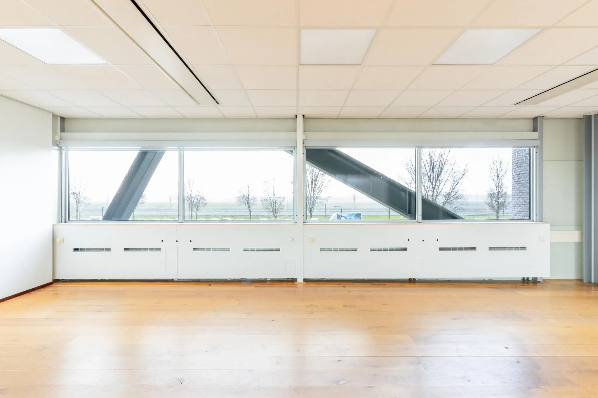 Lichte, lege kantoorruimte aan de Meidoornkade met houten vloer en grote ramen met uitzicht op buiten.
