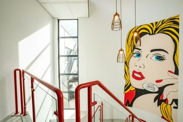 Trapopgang met rode leuningen, grote raampartij en een opvallende muurschildering in pop-art stijl met de tekst "Never a bridge too far".
