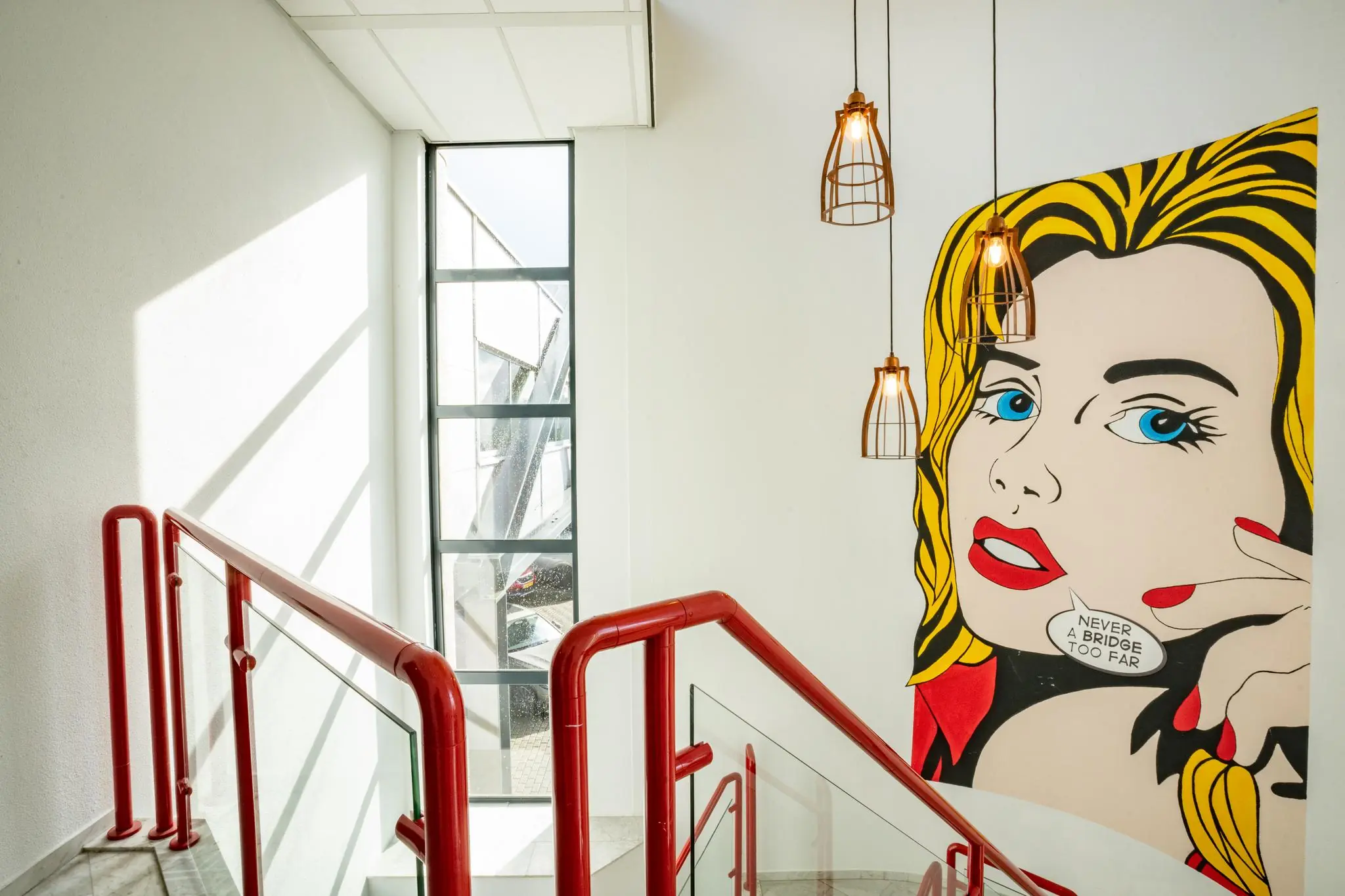 Trapopgang met rode leuningen, grote raampartij en een opvallende muurschildering in pop-art stijl met de tekst "Never a bridge too far".