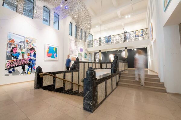 Licht en modern interieur van een kunstgalerie aan het Weesperplein met kleurrijke schilderijen en een marmeren trap.