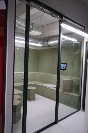 Glazen vergaderruimte op Weesperplein met terrazzo-zitbanken, zeshoekige krukken en een scherm aan de muur.