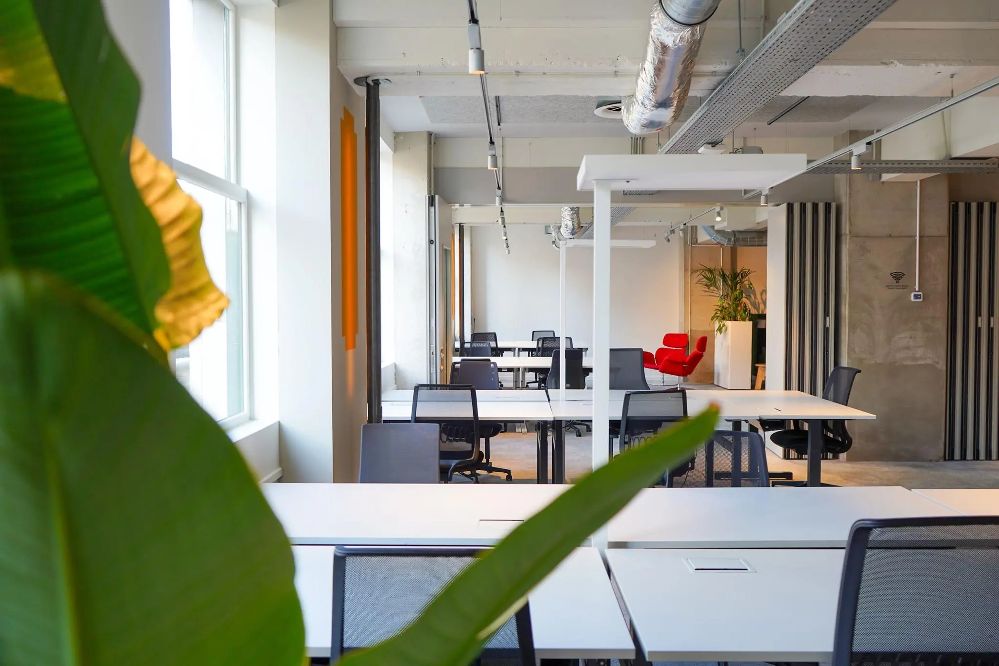Modern en licht kantoor op Weesperplein met flexwerkplekken, grote ramen, groene planten en een opvallende rode fauteuil achterin.