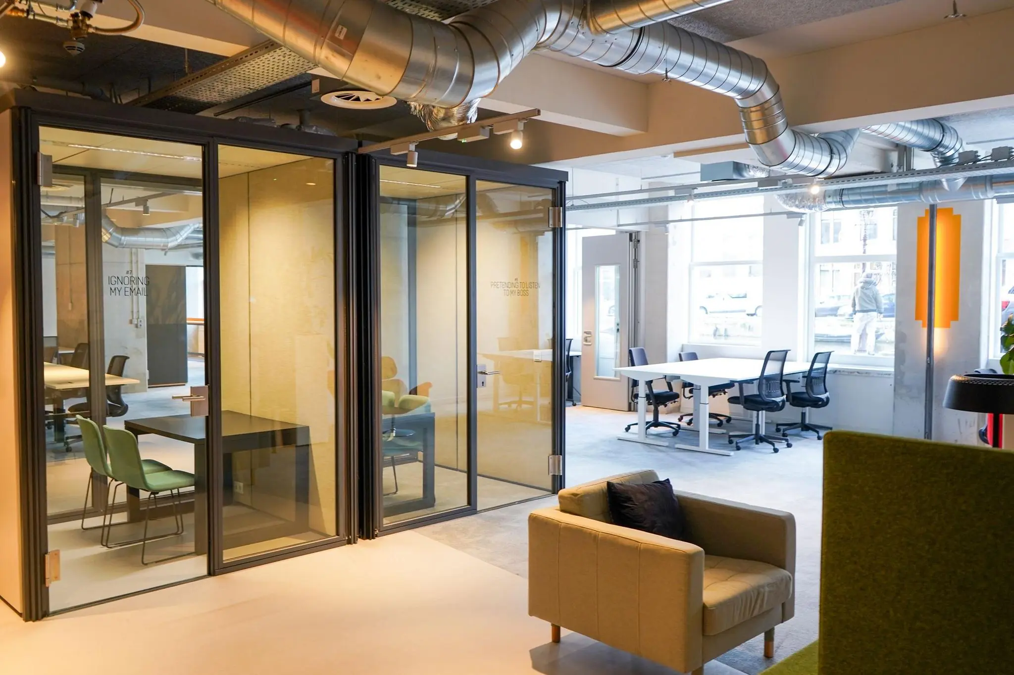 Moderne kantoorruimte op het Weesperplein met glazen vergaderruimtes, werkplekken en industriële plafonddetails.