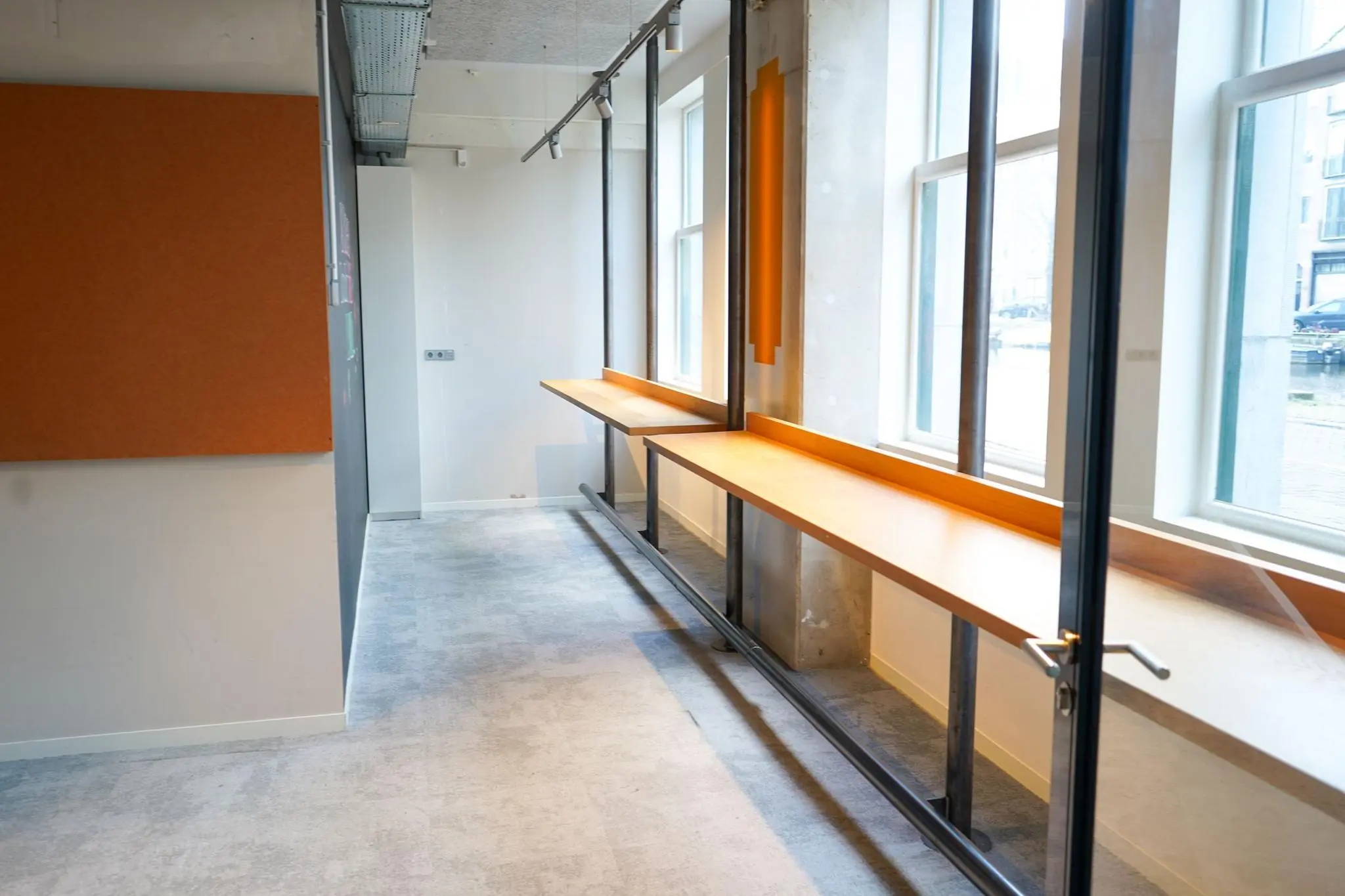 Lichte kantoorruimte aan het Weesperplein met lange houten werktafel langs grote ramen.