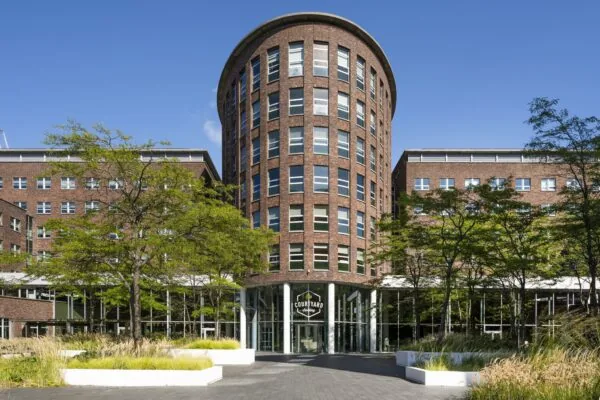 Vooraanzicht van het Courtyard by Marriott hotel aan de Orteliuslaan met een ronde toren en omliggende beplanting.