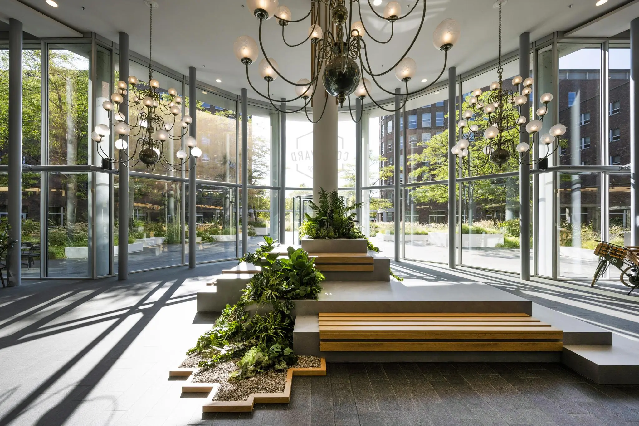 Moderne en lichte entreehal aan de Orteliuslaan met grote raampartijen, groene planten en designkroonluchters.