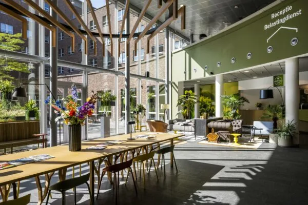 Moderne wachtruimte met veel daglicht, planten en zitgelegenheid in het belastingdienstkantoor aan de Orteliuslaan.
