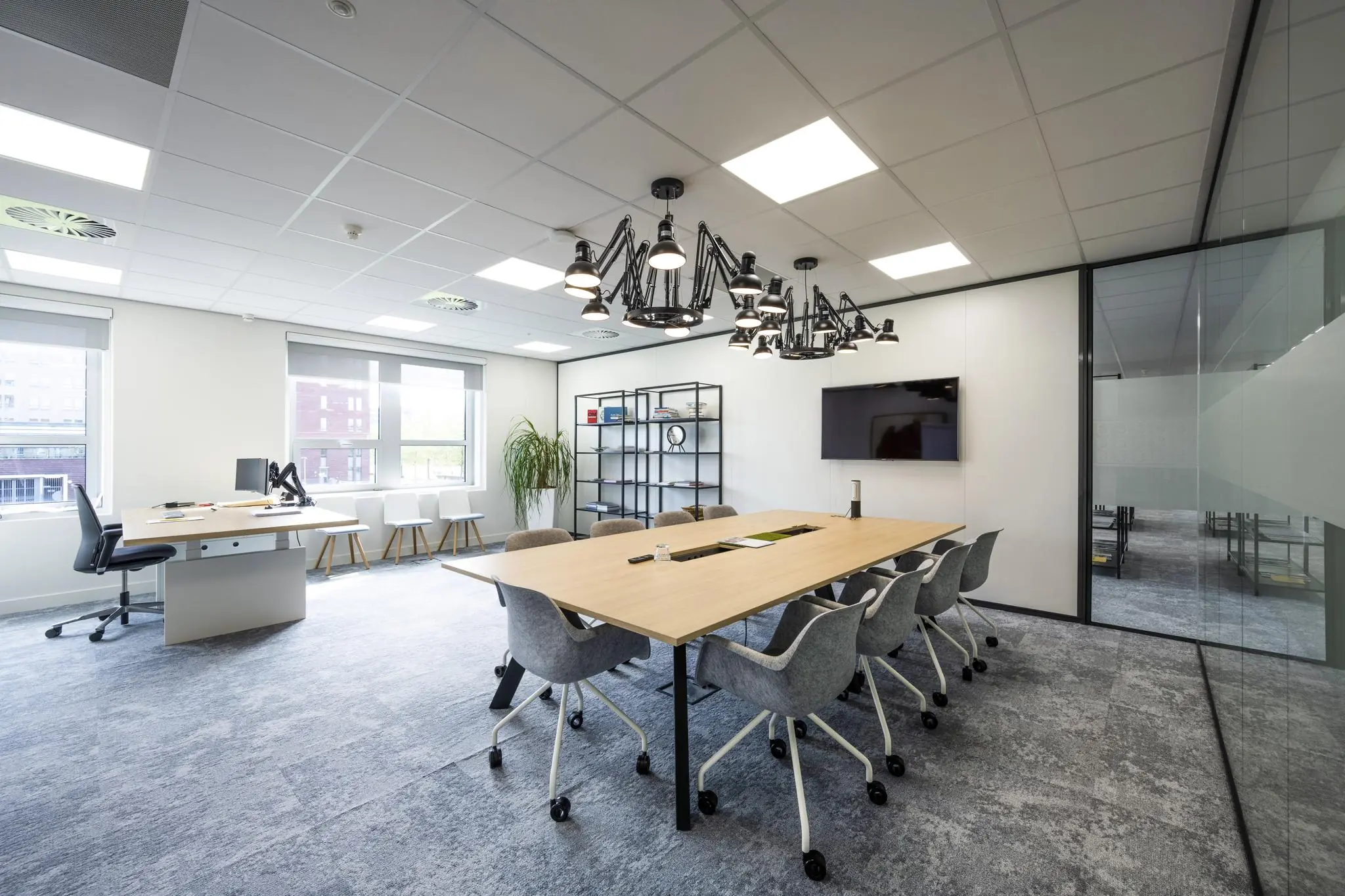 Moderne vergaderruimte aan de Orteliuslaan met een grote houten tafel, grijze stoelen op wieltjes, plafondverlichting en een flatscreen aan de wand.