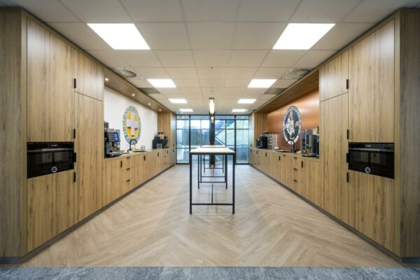 Moderne bedrijfskeuken aan de Orteliuslaan met houten kasten, koffieapparaten en zitruimte met hoge tafels.