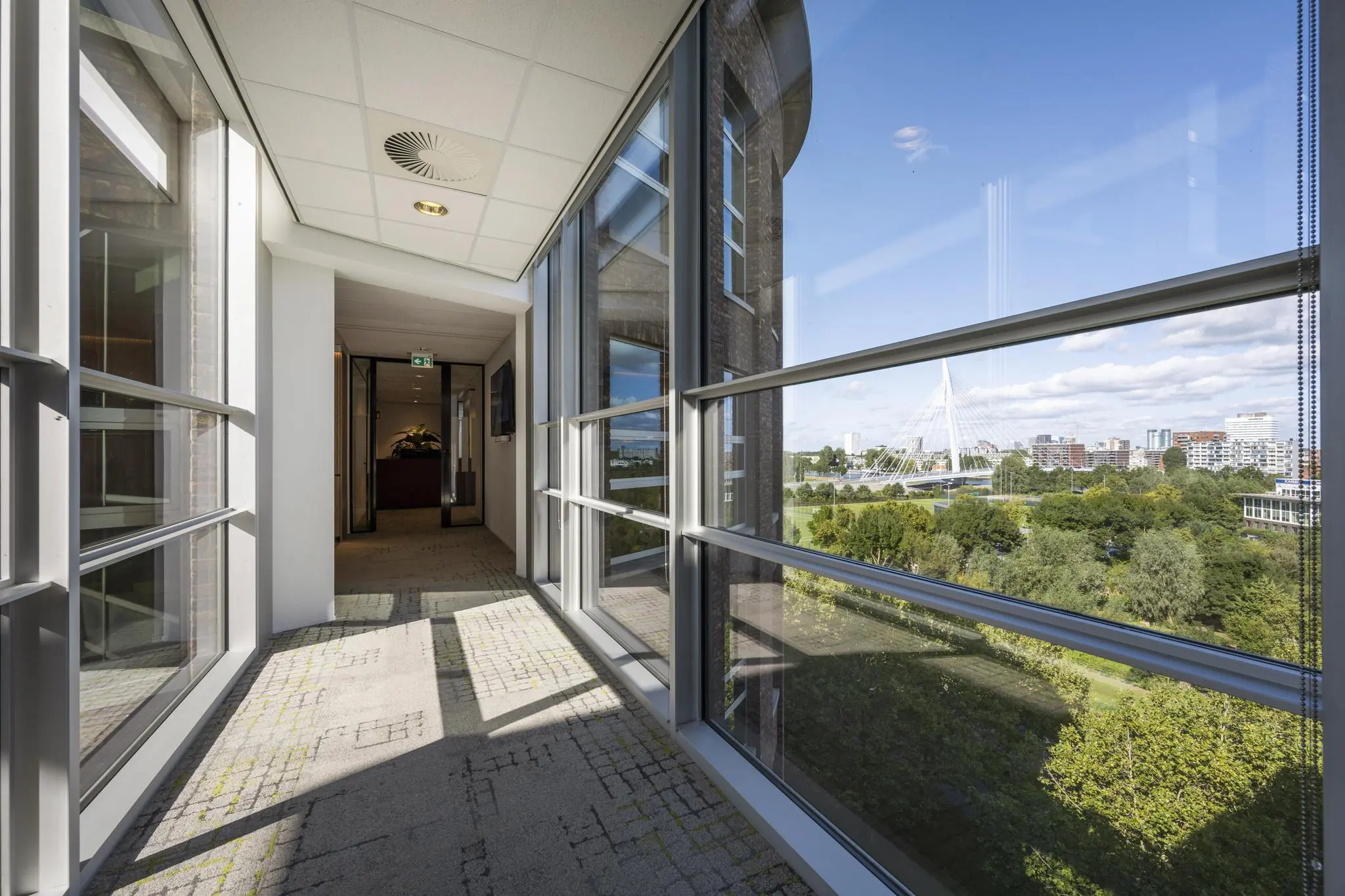Doorgang met glazen wanden in een kantoorpand aan de Orteliuslaan, met uitzicht op de Dafne Schippersbrug en de stad Utrecht.