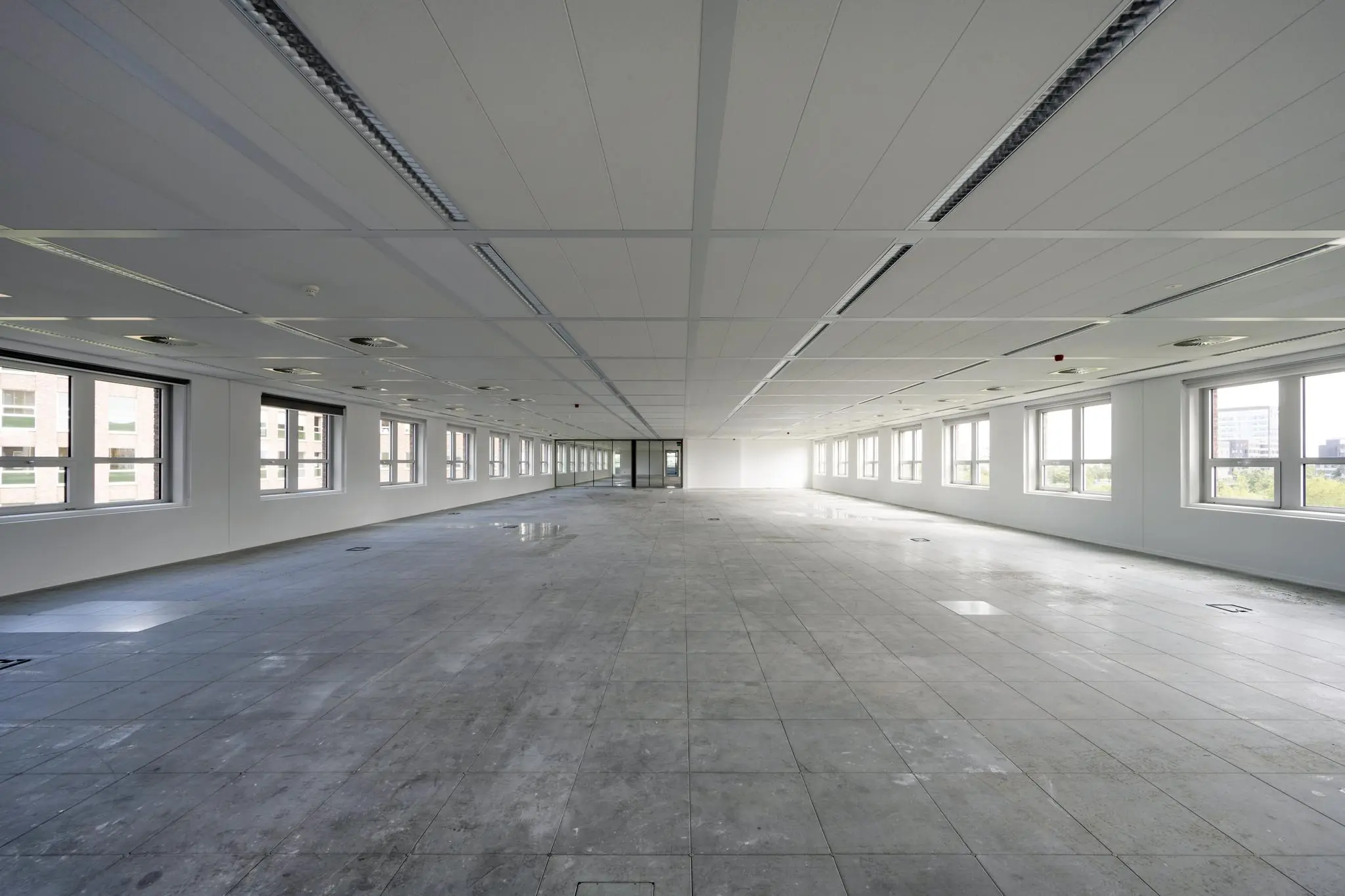 Leeg kantoorpand aan de Orteliuslaan met grote ramen en betonnen vloer.