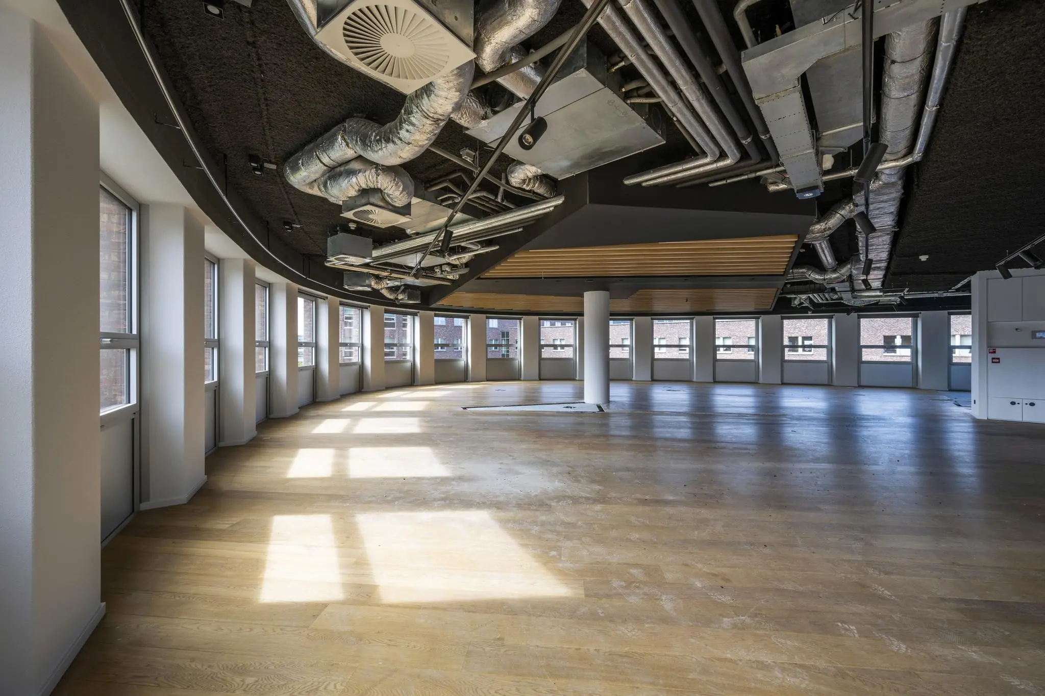 Leeg kantoorpand aan de Orteliuslaan met grote ramen, houten vloer en zichtbare plafondinstallaties.