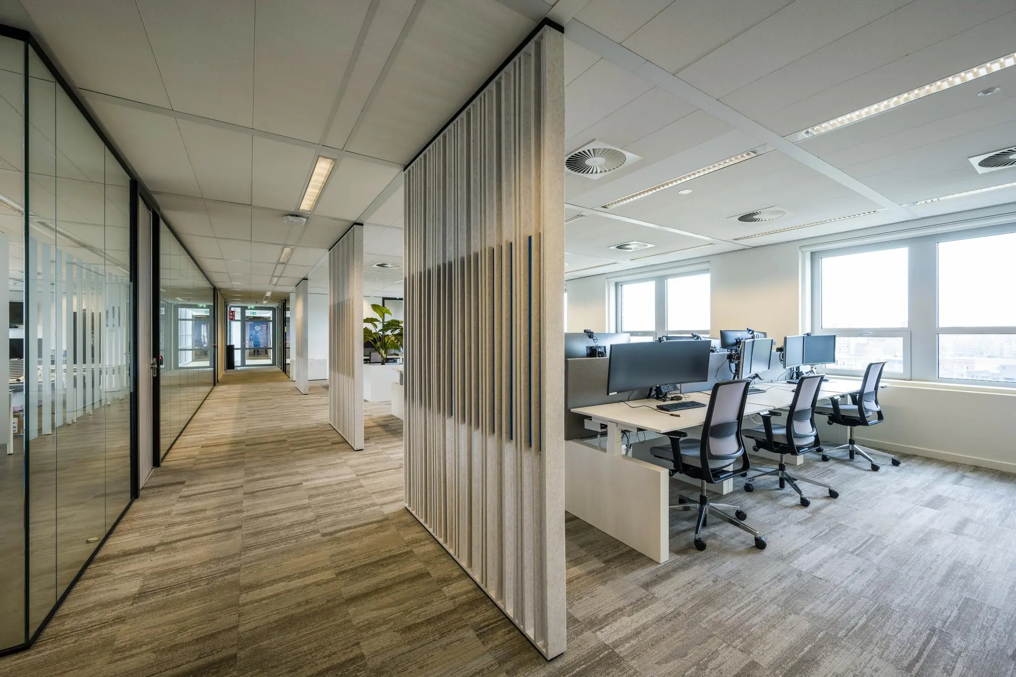 Modern kantoorinterieur aan de Orteliuslaan met glazen vergaderruimtes en werkplekken met bureaus en computerschermen.