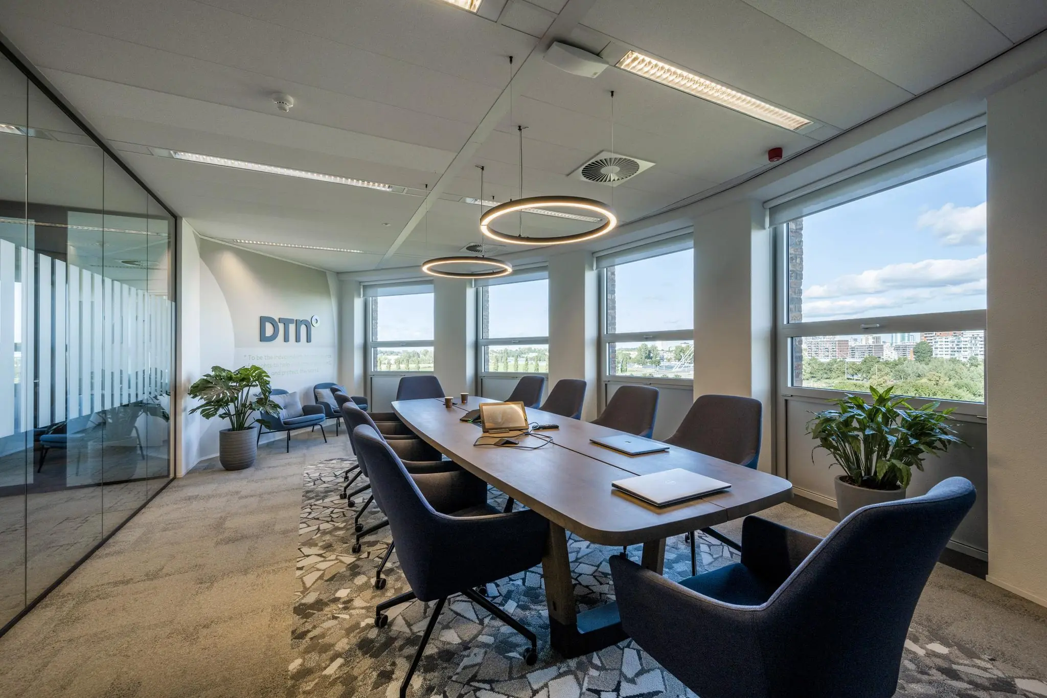 Moderne vergaderruimte bij DTN op de Orteliuslaan met een lange tafel, stoelen, laptops en grote ramen met uitzicht op de stad.
