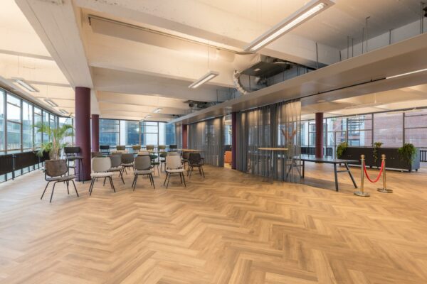 Moderne en ruime evenementen- of vergaderruimte aan de Vlasmarkt met houten visgraatvloer, diverse stoelen en glazen wanden met gordijnen.