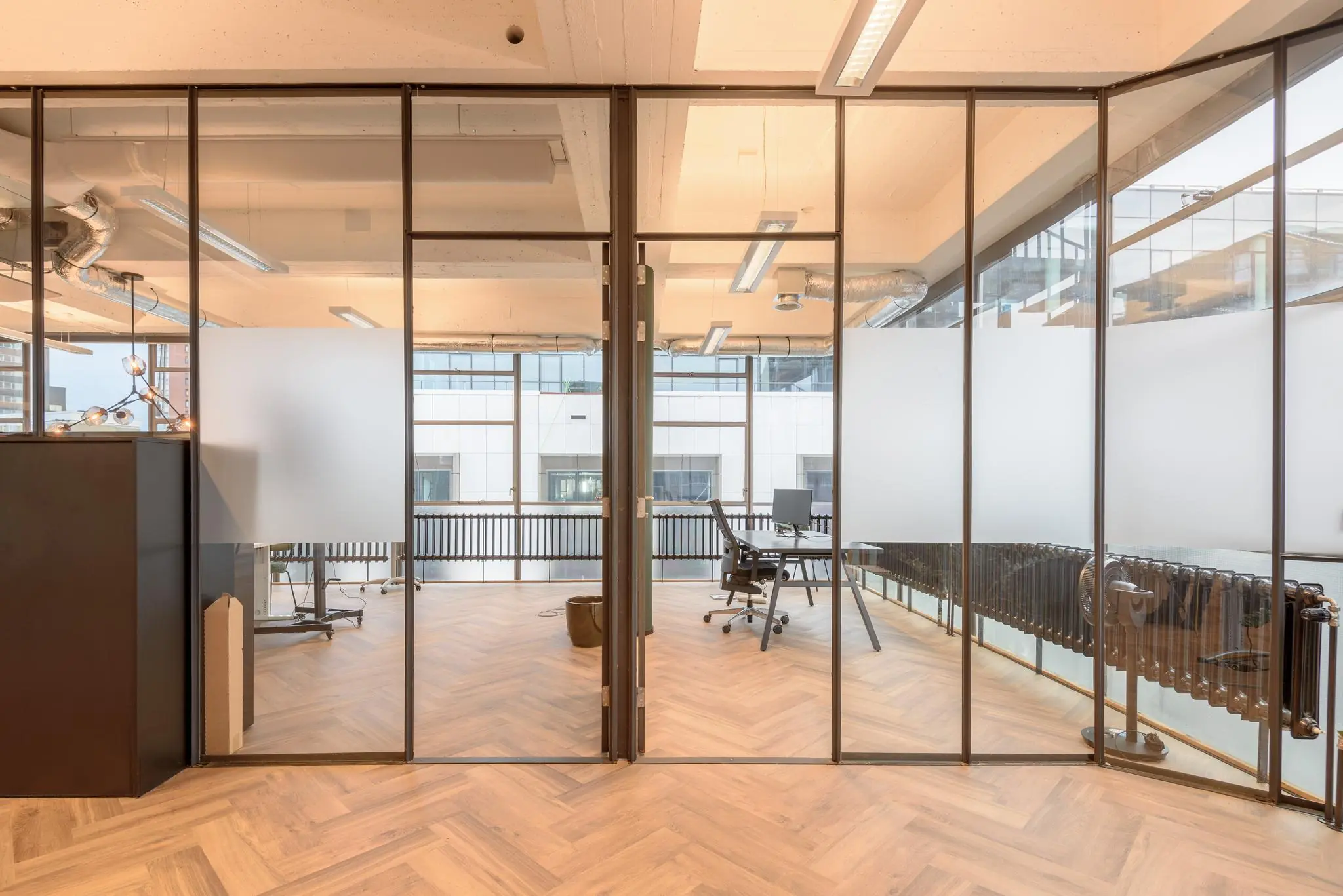 Modern kantoorinterieur aan de Vlasmarkt met glazen wanden, houten visgraatvloer en uitzicht op een stadspand.