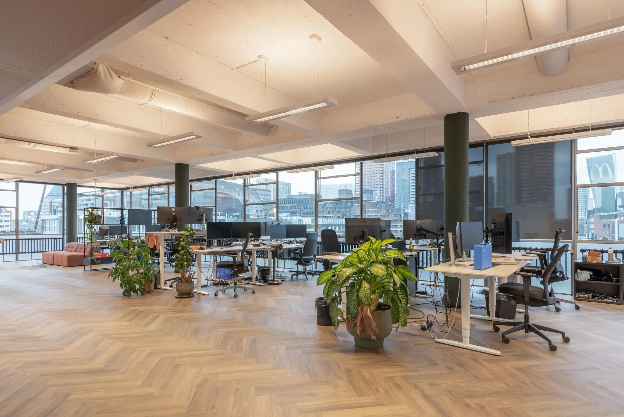Moderne open kantoorruimte aan de Vlasmarkt met houten vloer, bureaus, grote ramen en groene planten.