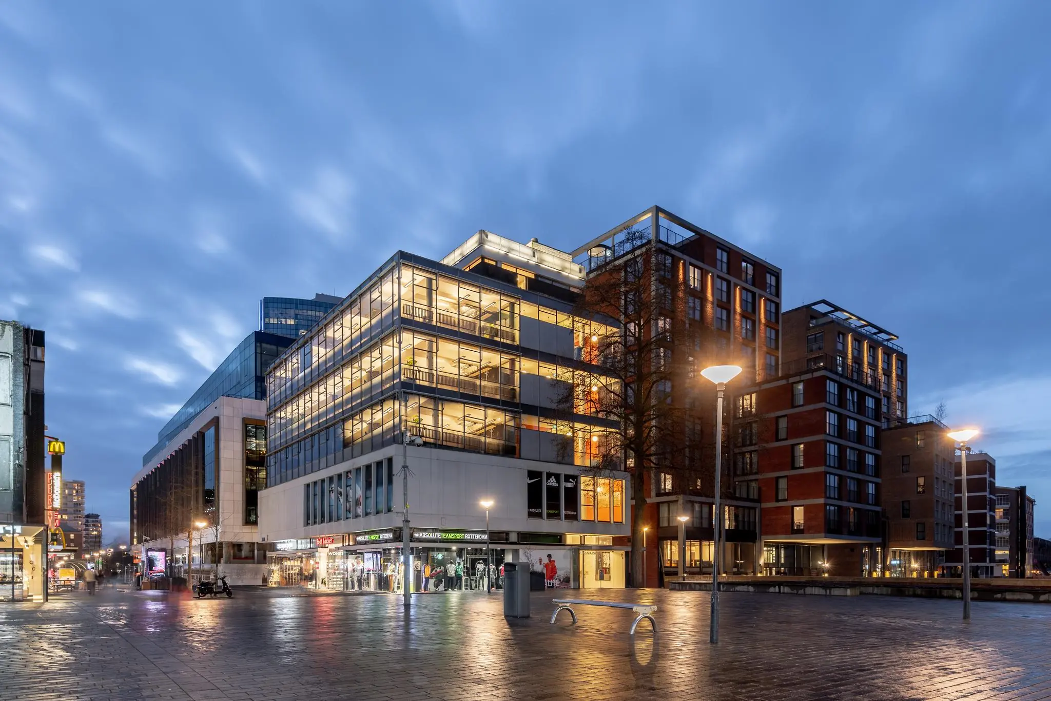 Avondbeeld van de Vlasmarkt in Rotterdam met moderne gebouwen en sfeerverlichting.
