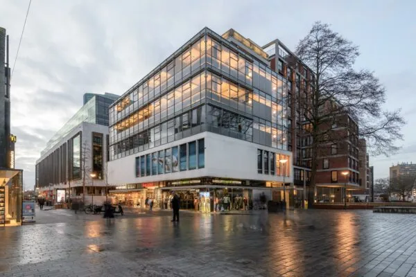 Modern winkelpand aan de Vlasmarkt in Rotterdam bij schemering met verlichte etalages en glazen gevel.
