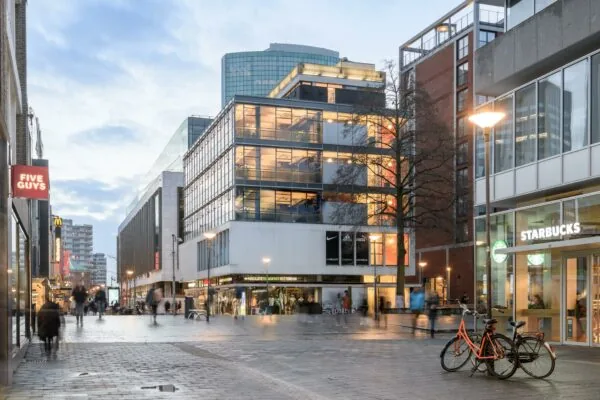 Drukke winkelstraat aan de Vlasmarkt in Rotterdam met onder andere Starbucks, Five Guys en sportwinkels in moderne gebouwen.