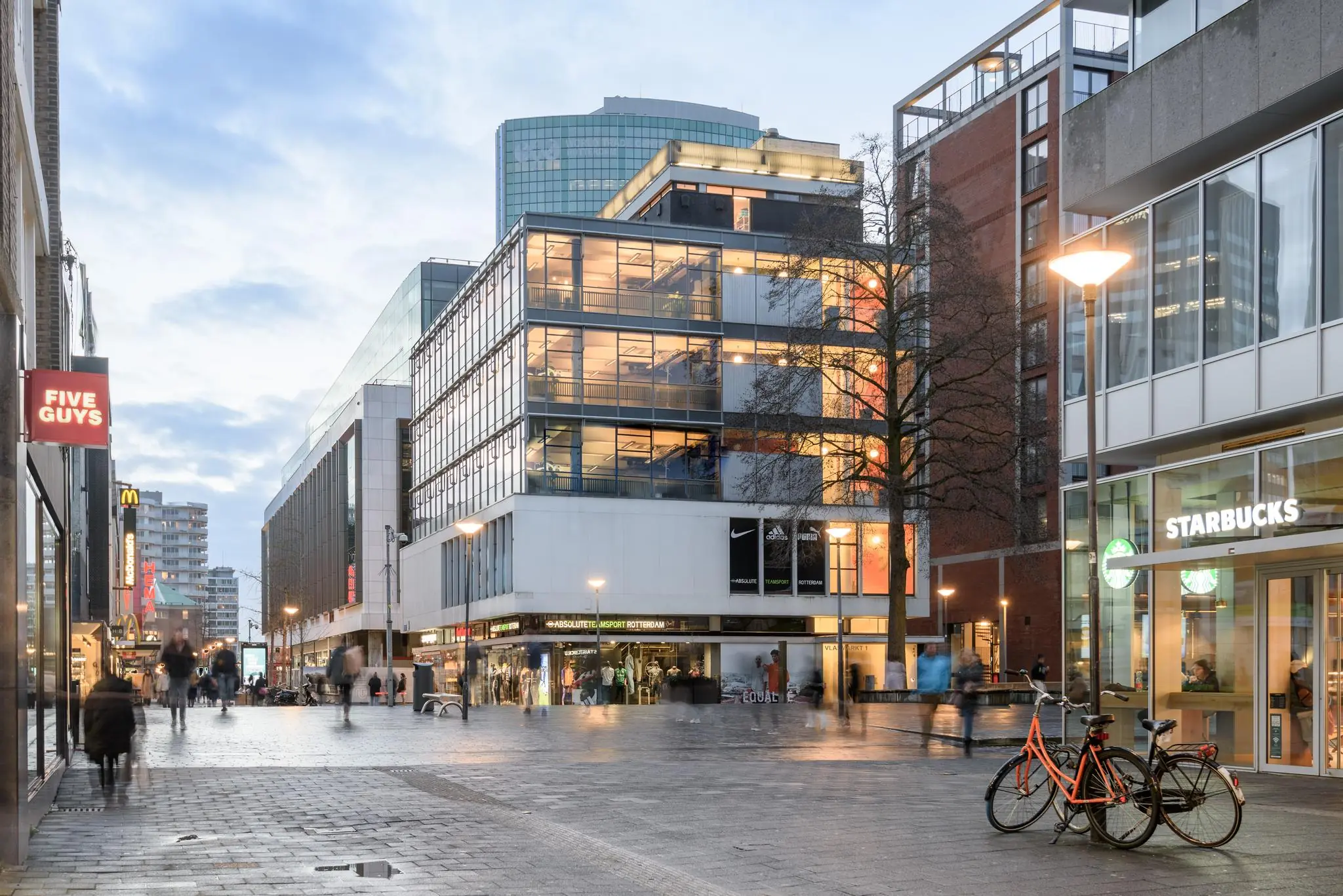 Drukke winkelstraat aan de Vlasmarkt in Rotterdam met onder andere Starbucks, Five Guys en sportwinkels in moderne gebouwen.