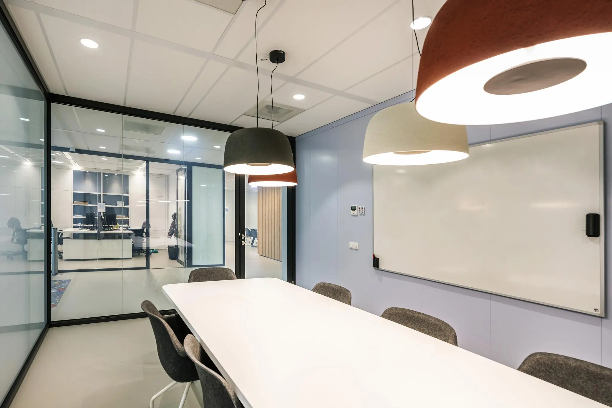 Moderne vergaderruimte aan de Paalbergweg met glazen wanden, een witte vergadertafel, grijze stoelen, hanglampen en een whiteboard.