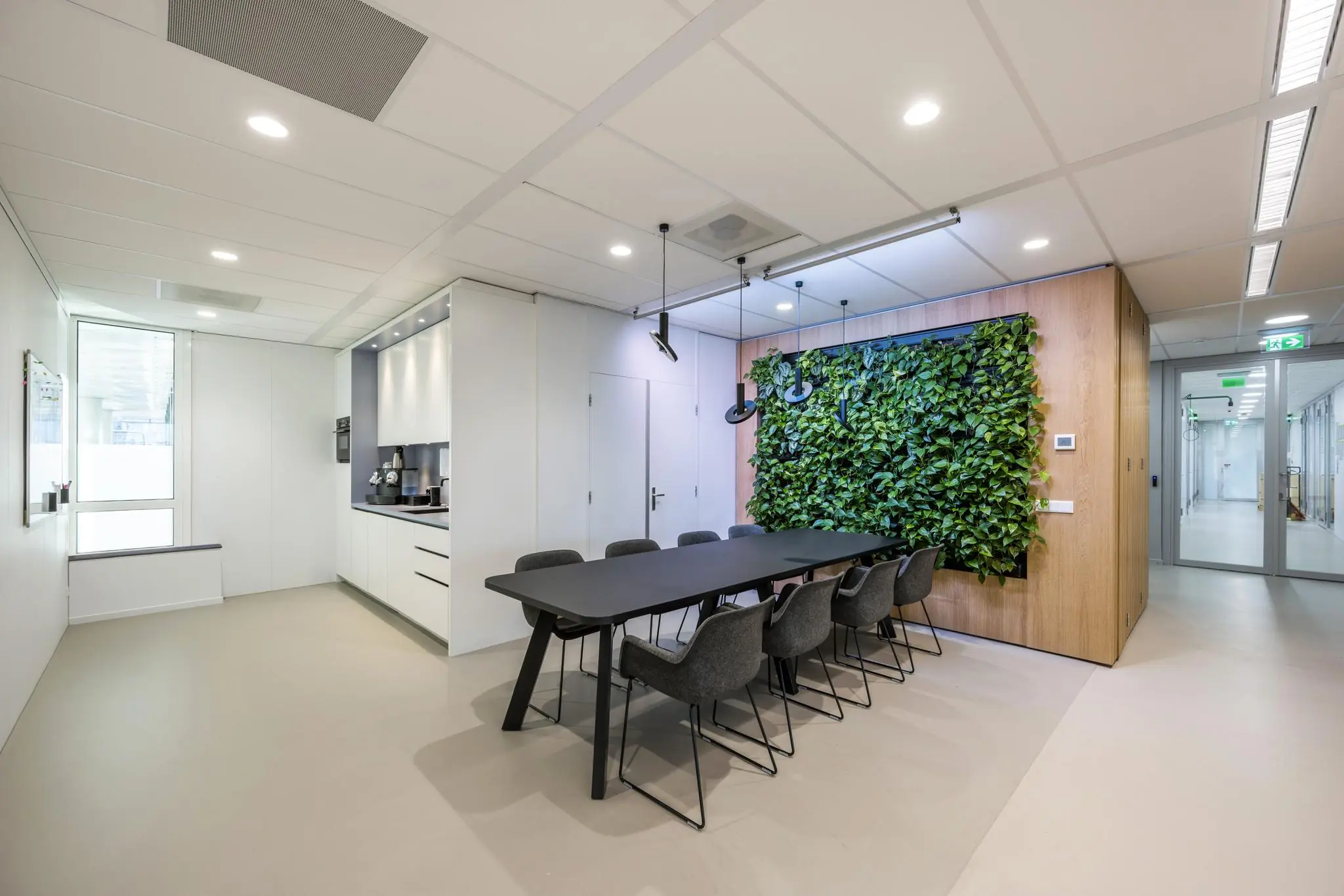 Moderne vergaderruimte aan de Paalbergweg met een lange tafel, grijze stoelen, groene plantenwand en een kitchenette.