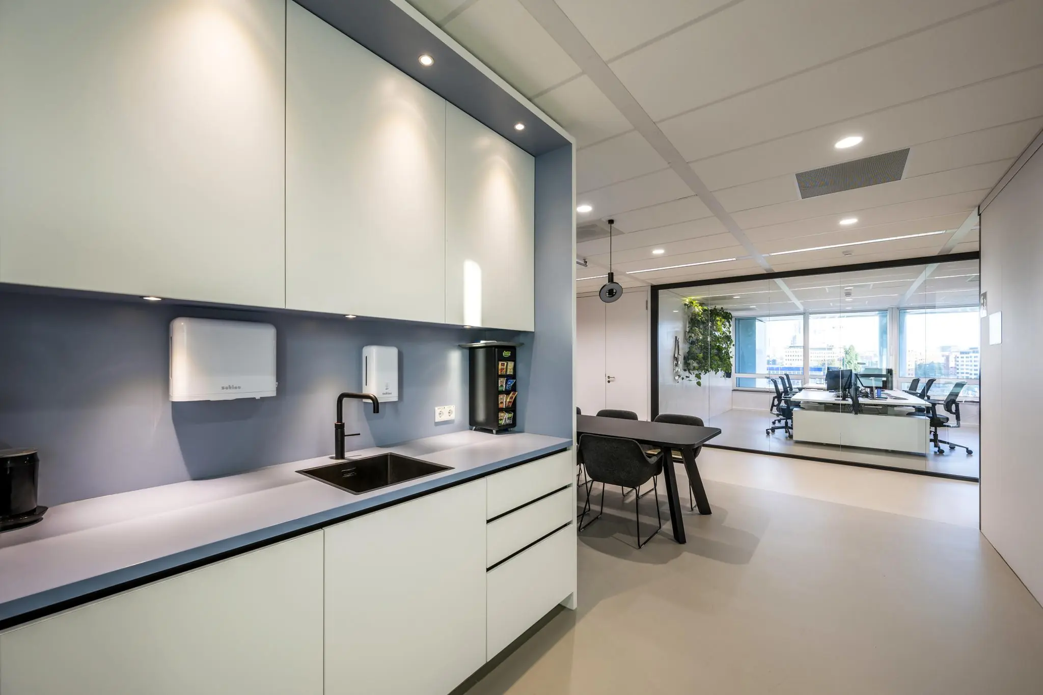 Moderne kantoorruimte aan de Paalbergweg met open keuken, vergadertafel en glazen wand met uitzicht op werkplekken.