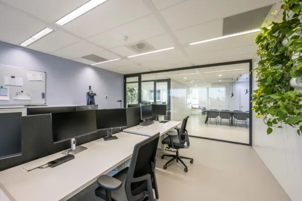 Moderne kantoorruimte aan de Paalbergweg met werkplekken, glazen vergaderruimte en groene muurdecoratie.