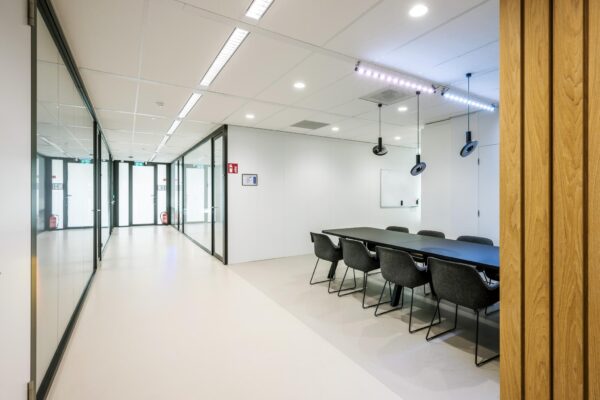 Moderne vergaderruimte aan de Paalbergweg met glazen wanden, zwarte tafel en grijze stoelen.