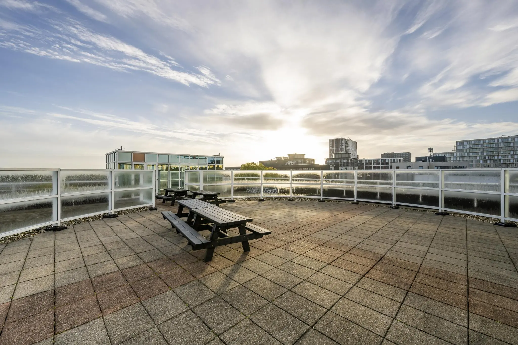 Ruim dakterras aan de Paalbergweg met picknickbanken en uitzicht op moderne kantoorgebouwen bij zonsopkomst.