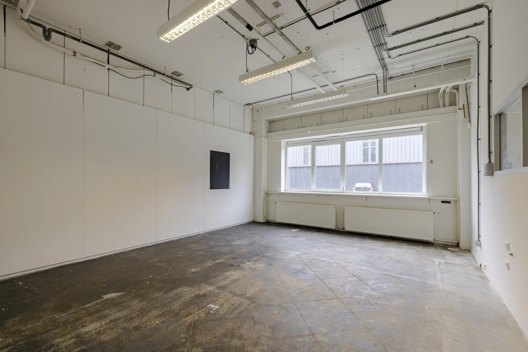 Leeg industrieel kantoorpand aan de Laarderhoogtweg met betonnen vloer, systeemplafond en groot raam.