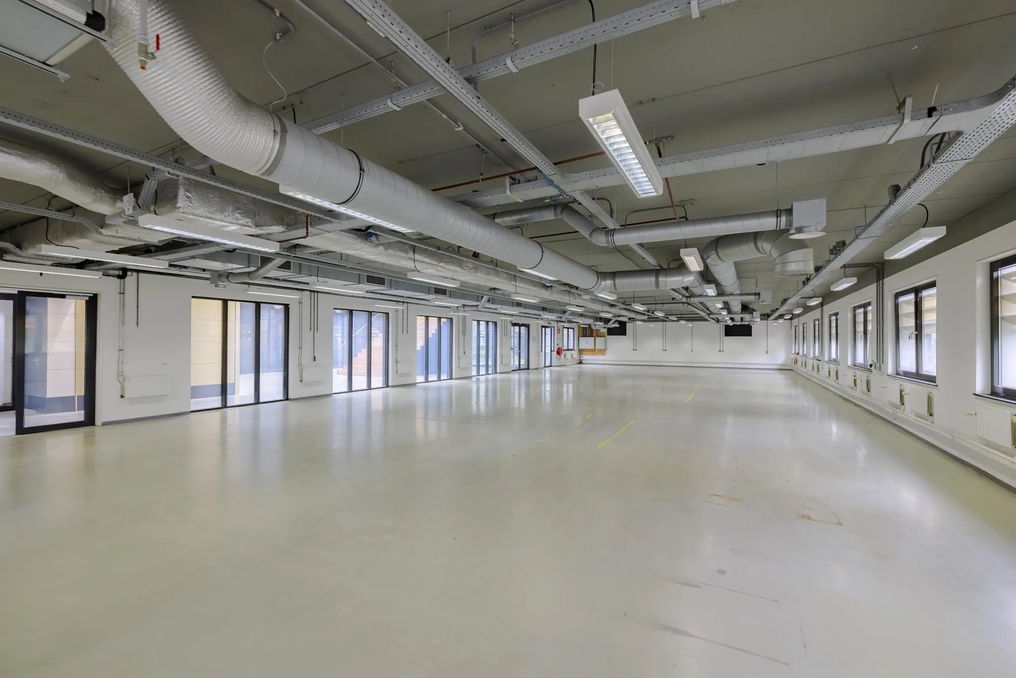Lege, industriële kantoorruimte aan de Laarderhoogtweg met zicht op grote ramen en zichtbare ventilatiebuizen aan het plafond.