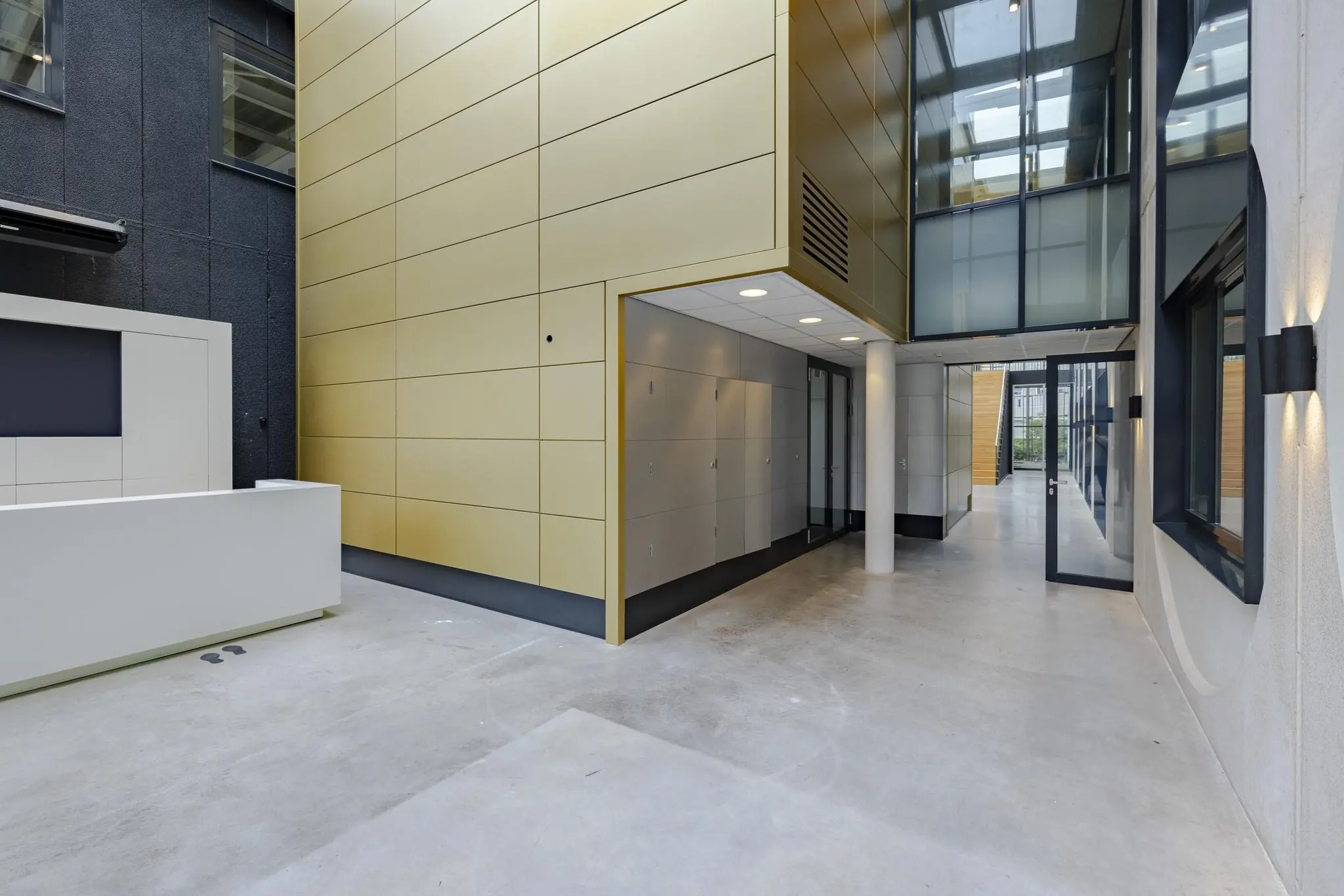 Moderne entreehal van een kantoorgebouw aan de Laarderhoogtweg met strakke lijnen, glazen deuren en goudkleurige gevelpanelen.