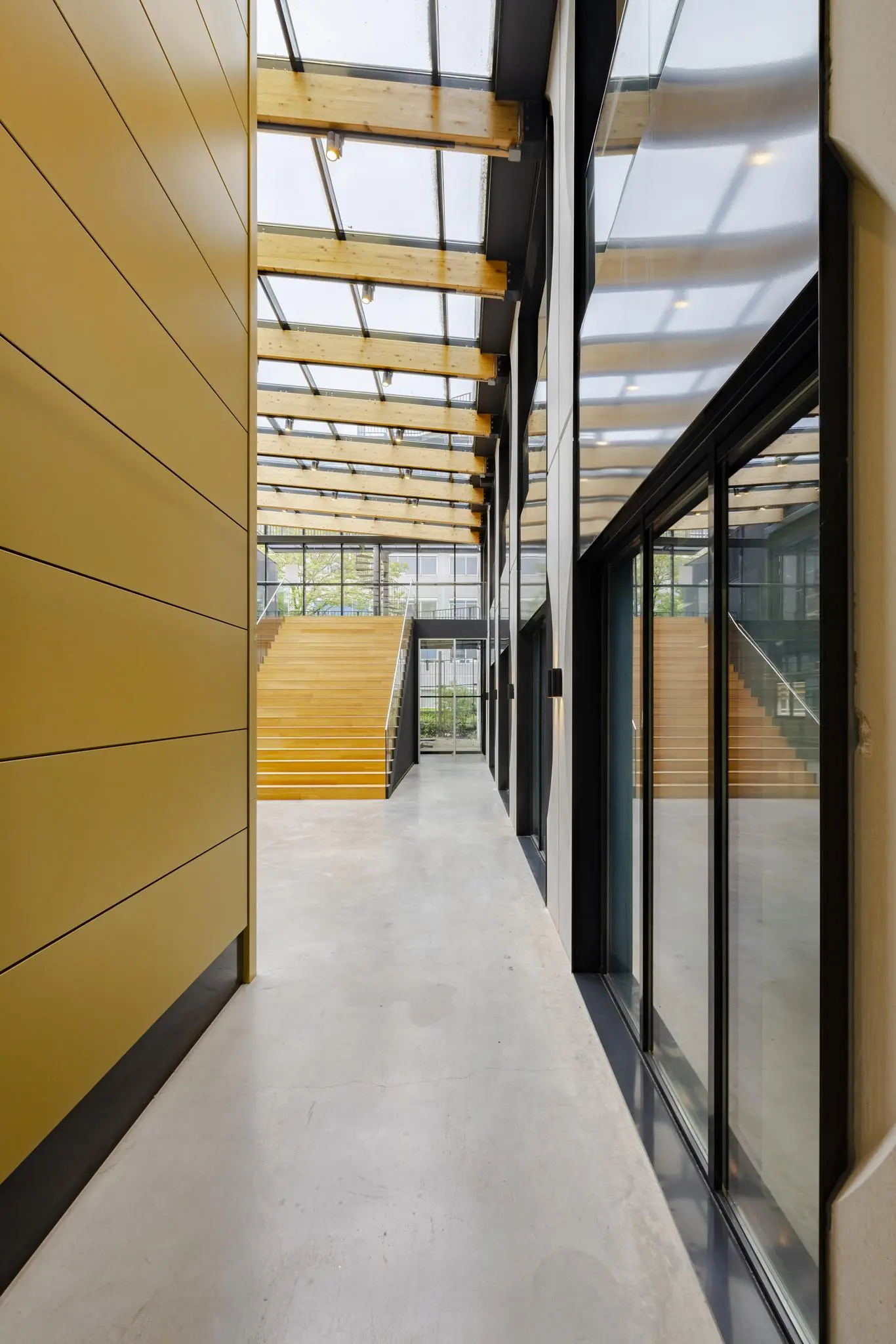 Moderne lichte binnenruimte aan de Laarderhoogtweg met houten trap, glazen dak en geel beklede wand.