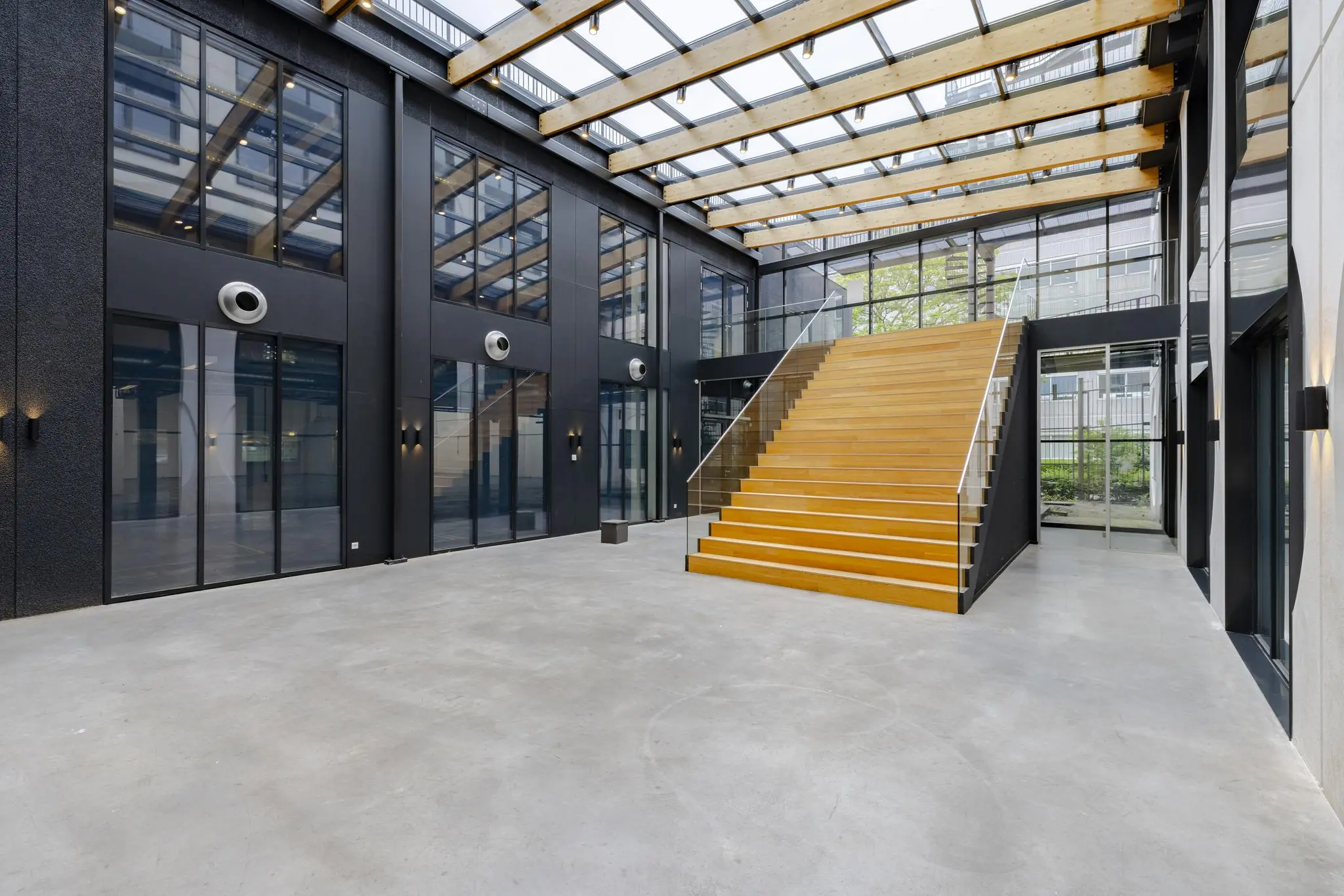 Moderne entreehal aan de Laarderhoogtweg met glazen dak, zwarte gevels en brede houten trap.