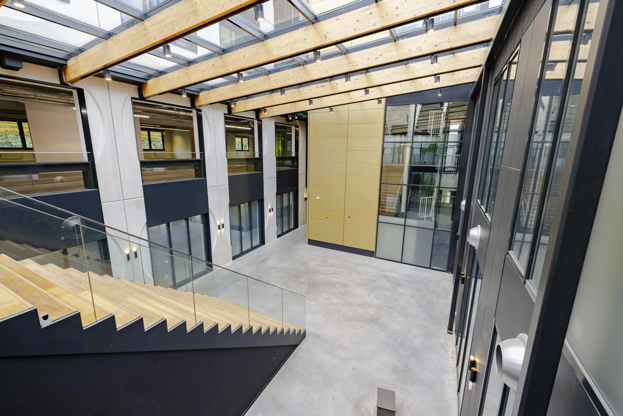 Moderne en lichte binnenruimte aan de Laarderhoogtweg met glazen dak, houten draagbalken en brede trap.