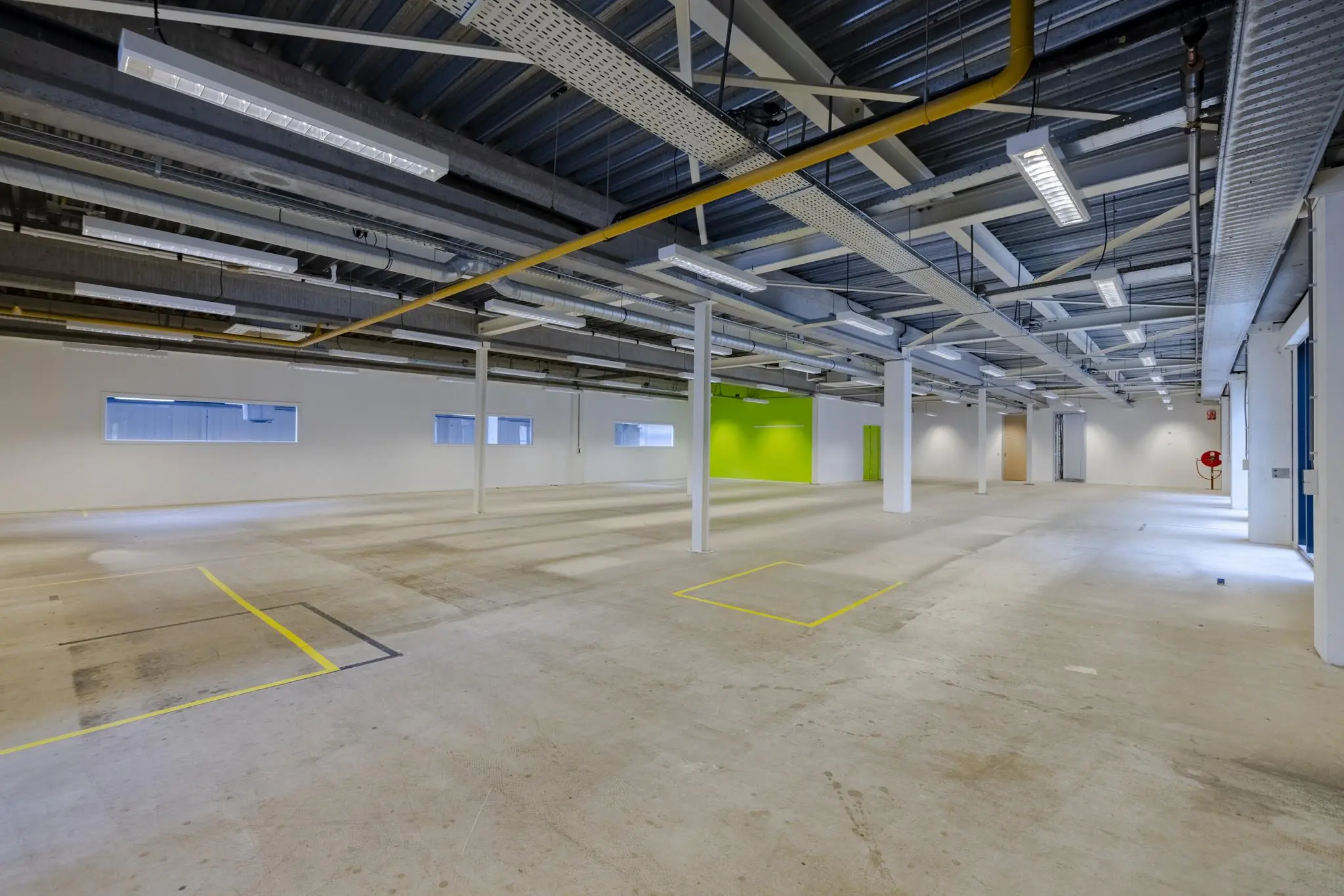 Leeg industrieel bedrijfsruimte-interieur aan de Laarderhoogtweg met betonnen vloer, zichtbare leidingen en felgroene wand.