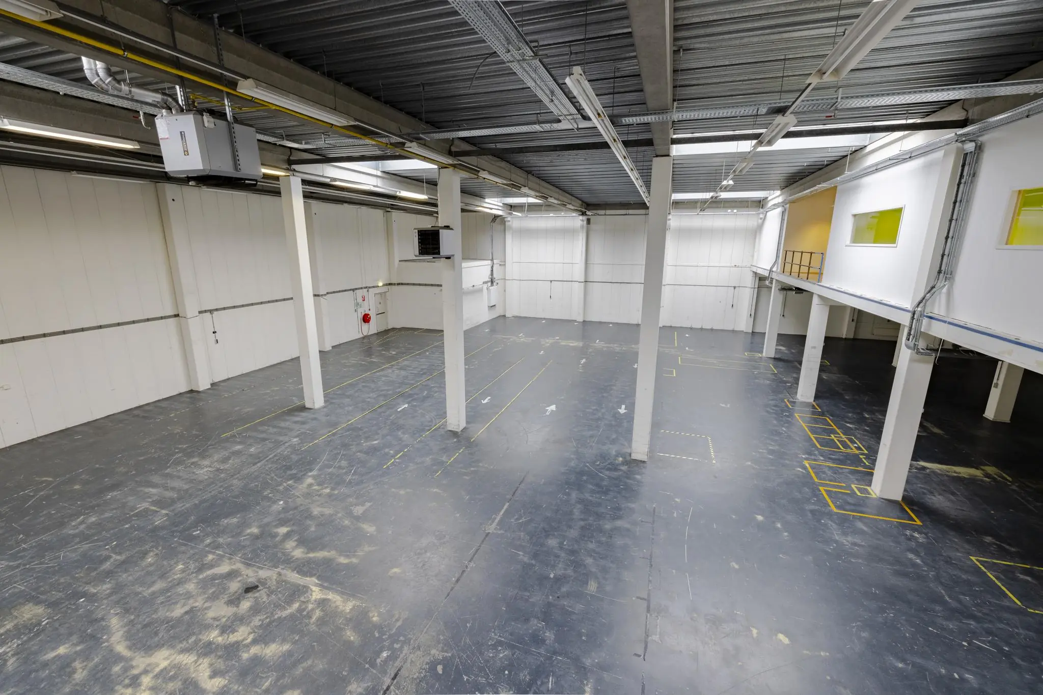 Lege industriële bedrijfsruimte aan de Laarderhoogtweg met betonnen vloer, witte wanden en entresol.